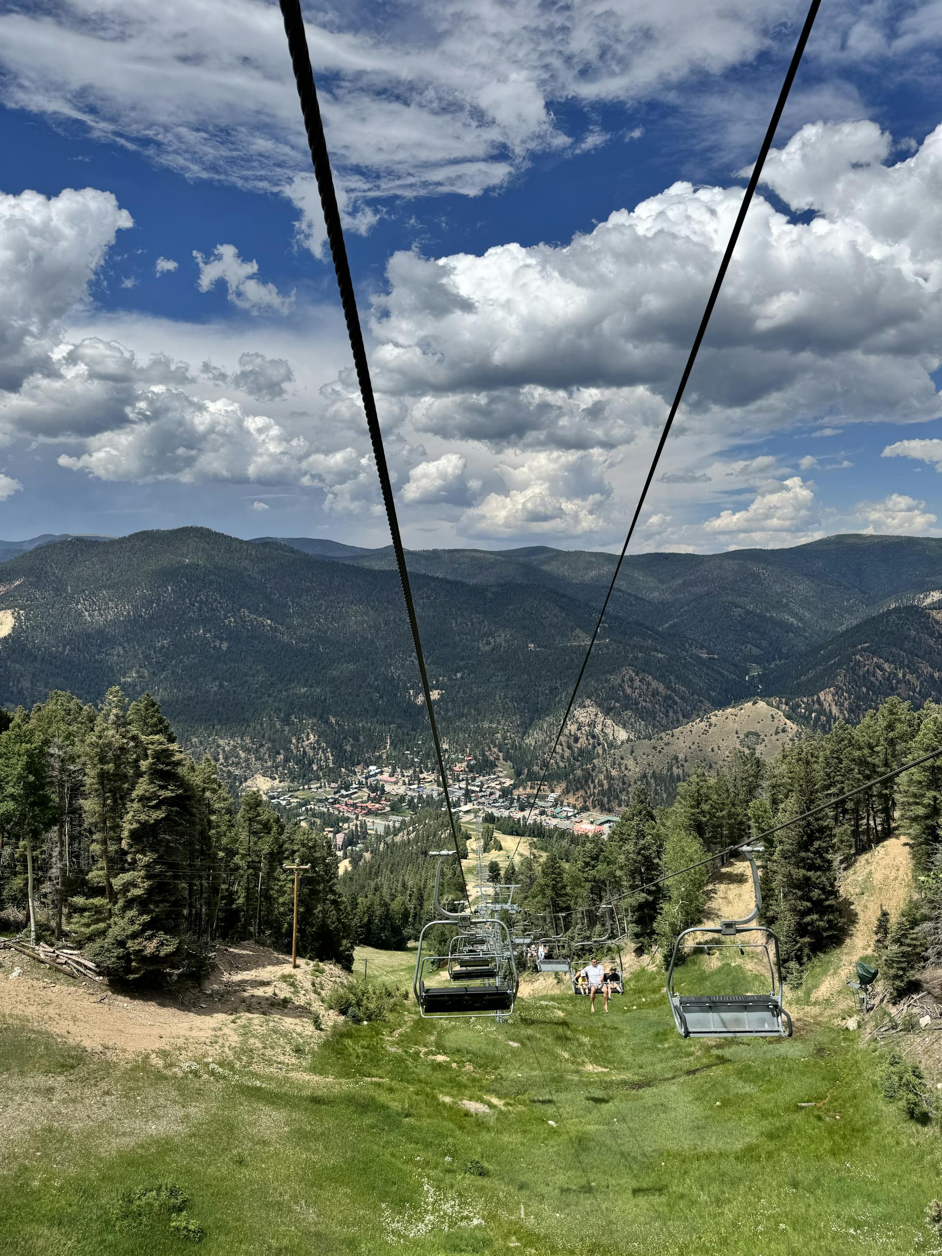 Chairlift ride above lush mountainous terrain in New Mexico under a vibrant blue sky.
